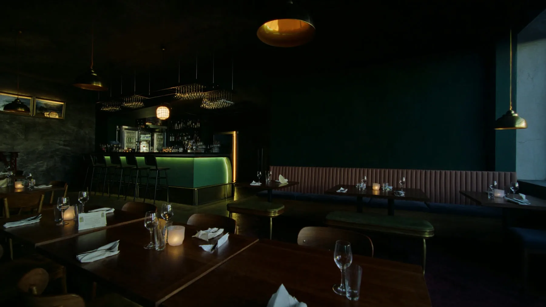 A restaurant dining room at dusk, tables set, bar lit behind