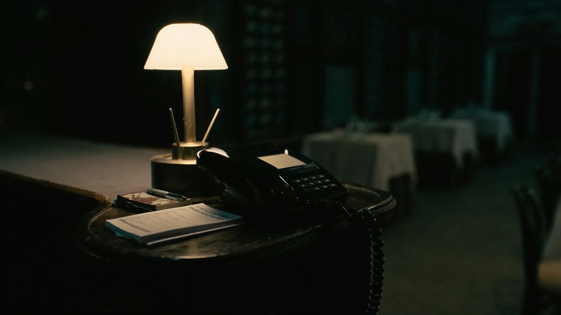 A telephone on an empty restaurant host stand under a lamp in the evening