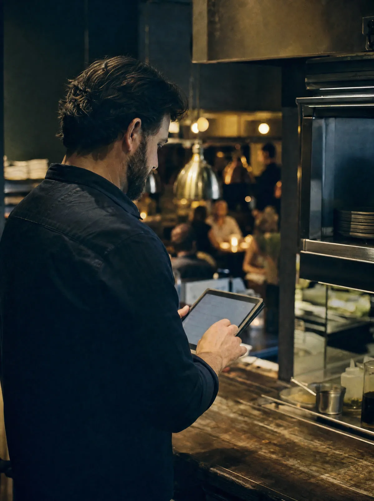 A restaurant manager reviewing the night's calls on a tablet at the pass